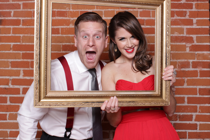 Two individuals making silly faces with a photo frame prop