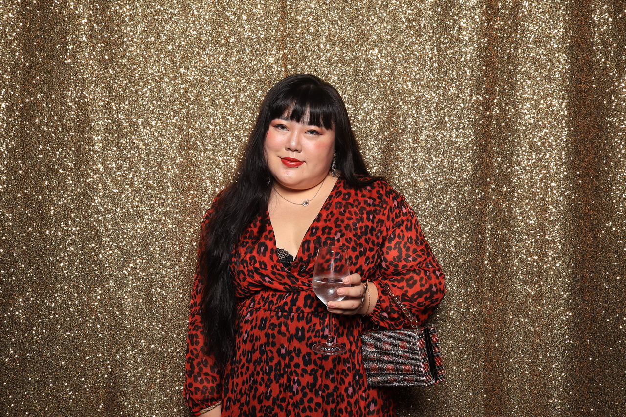 A guest in a red dress holding a glass of wine at the gold backdrop AI photo booth at Fairmont Century Plaza