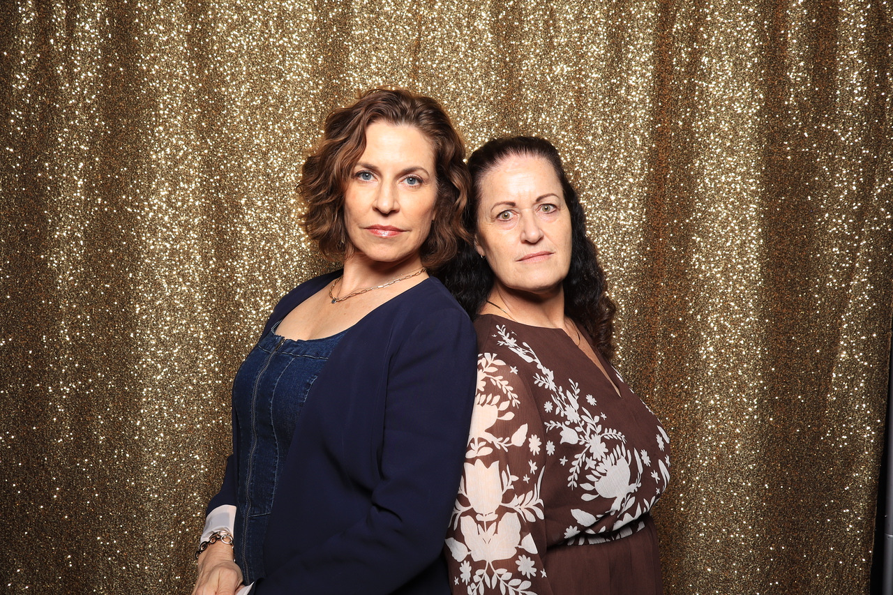 Two guests posing back to back in front of a gold sequin backdrop at the anniversary party AI photo booth in Los Angeles